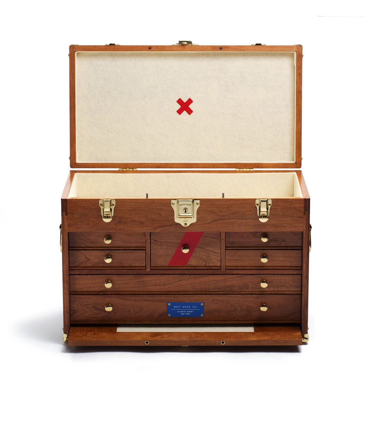 A wooden chest with its lid open, revealing multiple small drawers and compartments inside. The chest has brass fittings and a blue label on the front.