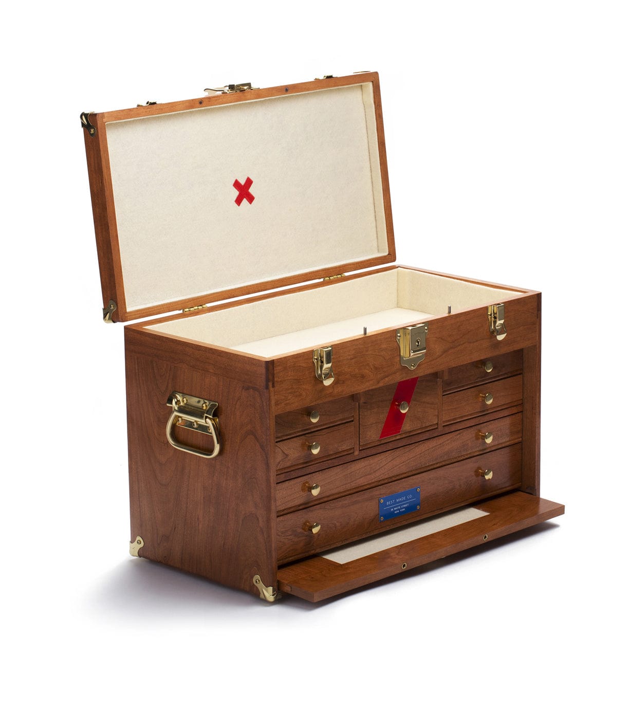 An open wooden toolbox with brass handles and locks, containing multiple drawers for organizing tools. The interior lid displays a red X mark.