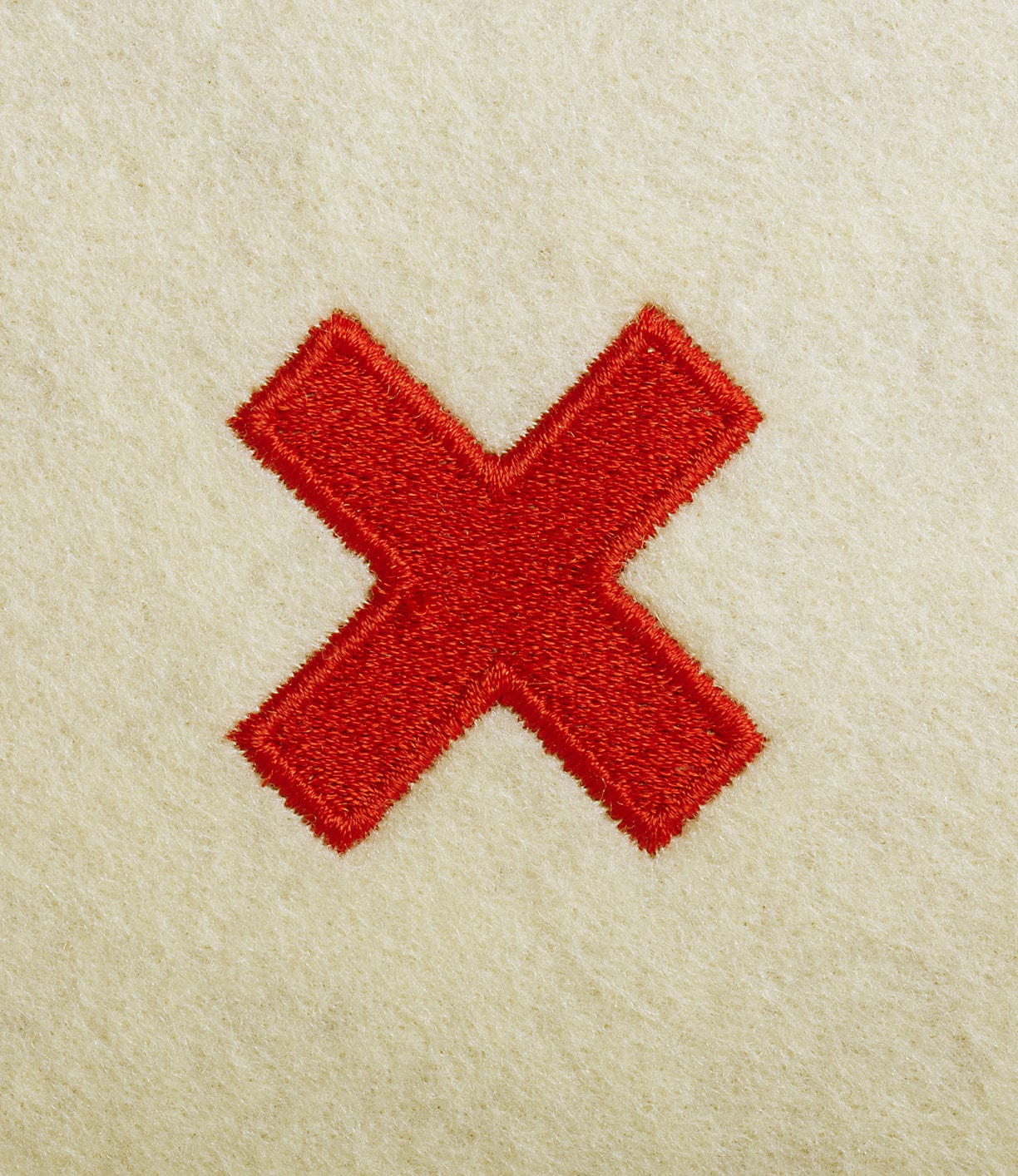 Red embroidered cross on a beige fabric background.