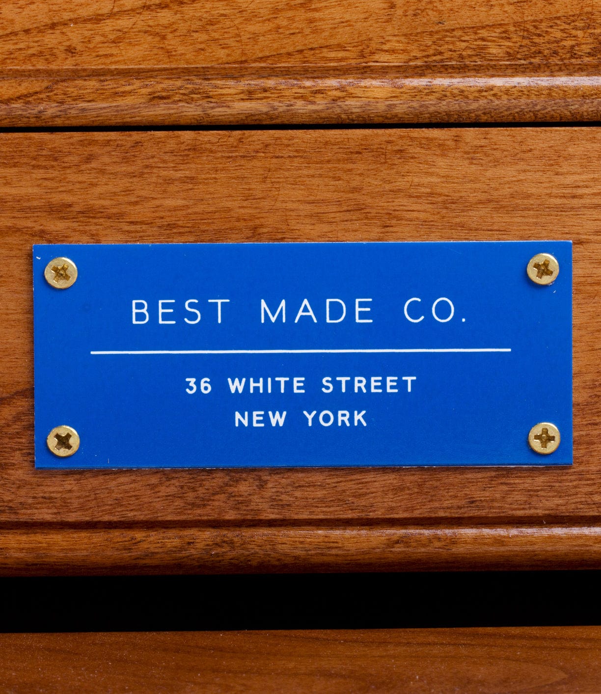 A blue metal plaque on a wooden surface reads BEST MADE CO. 36 WHITE STREET NEW YORK with four screws at the corners.