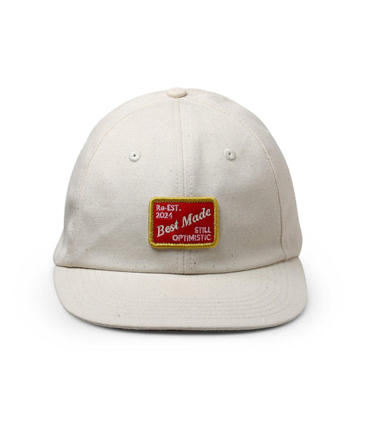 A beige baseball cap with a red and yellow embroidered patch that reads Re-EST. 2021 Best Made STILL OPTIMISTIC.