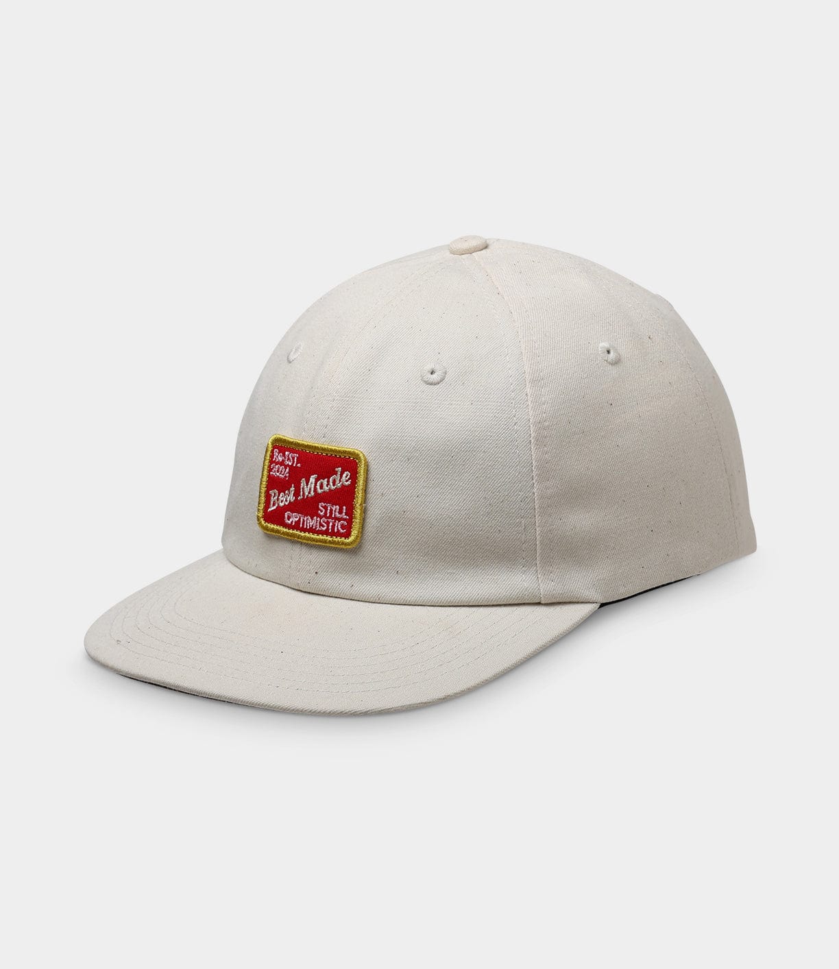 A beige baseball cap with a red and yellow patch on the front. The patch reads, The Best is Yet to Come, Best Made, and I'm Still Optimistic.