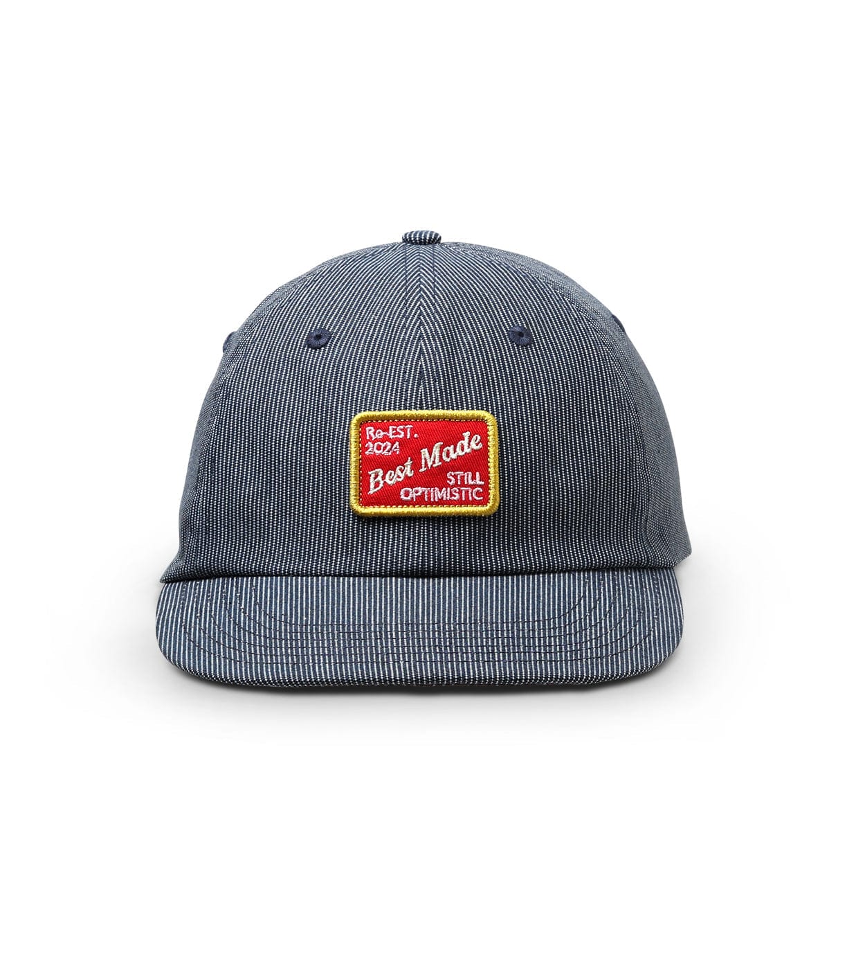 A blue-striped baseball cap with a front patch reading Re-EST. 2024 Best Made STILL OPTIMISTIC in red and yellow.