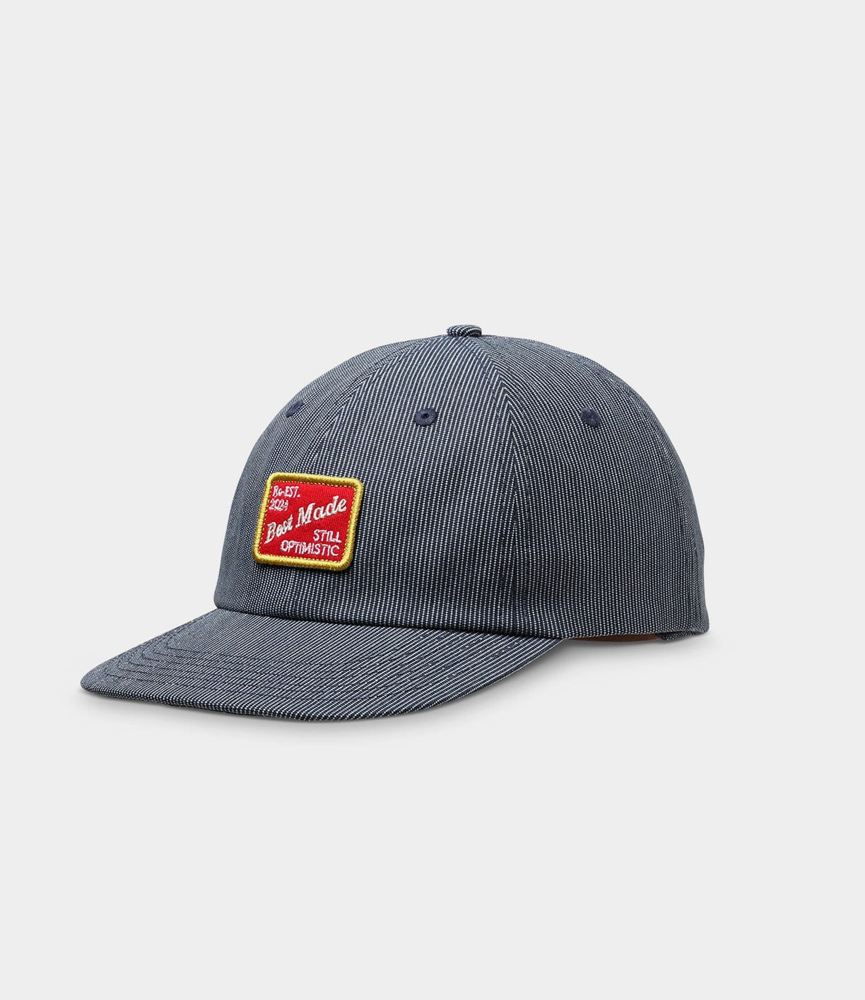 Dark blue baseball cap with white pinstripes. Features a rectangular patch on the front with red, yellow, and white text that reads If It. My Good Made Still Optimistic.