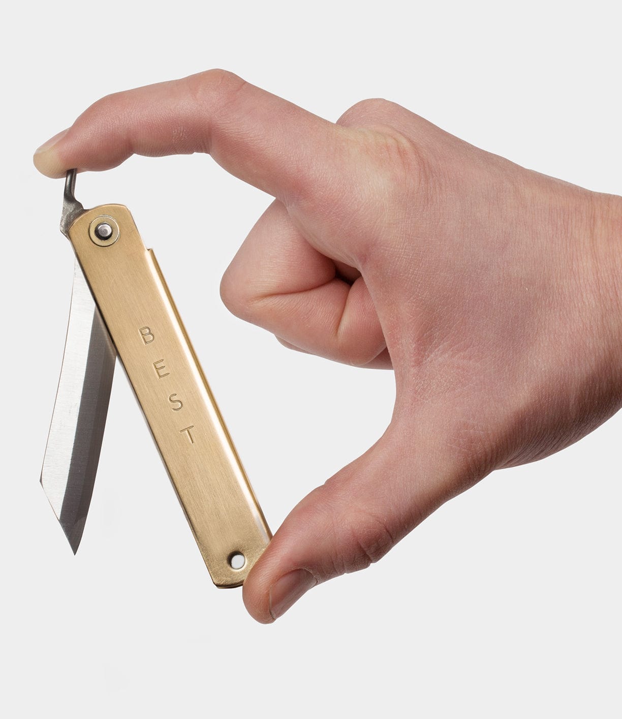 A hand holding a small folding knife with a brass handle and the word BEST engraved on it.