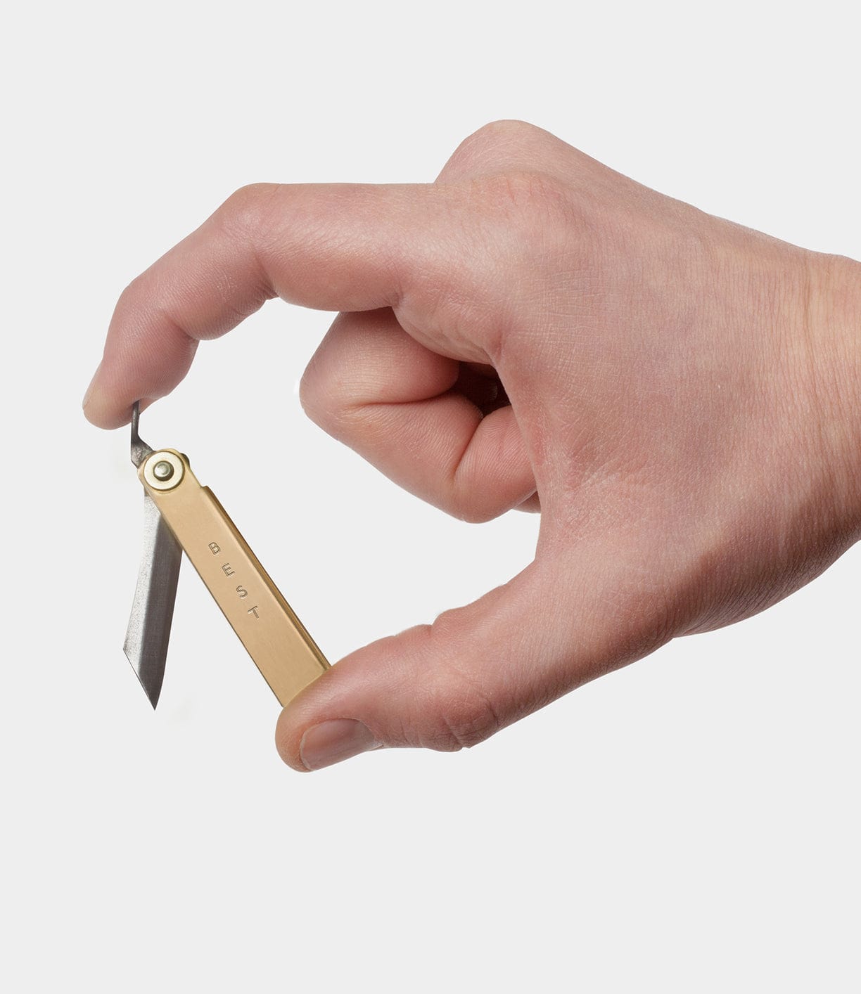 A hand holding a small brass utility knife with the blade extended. The word BEST is engraved on the side.