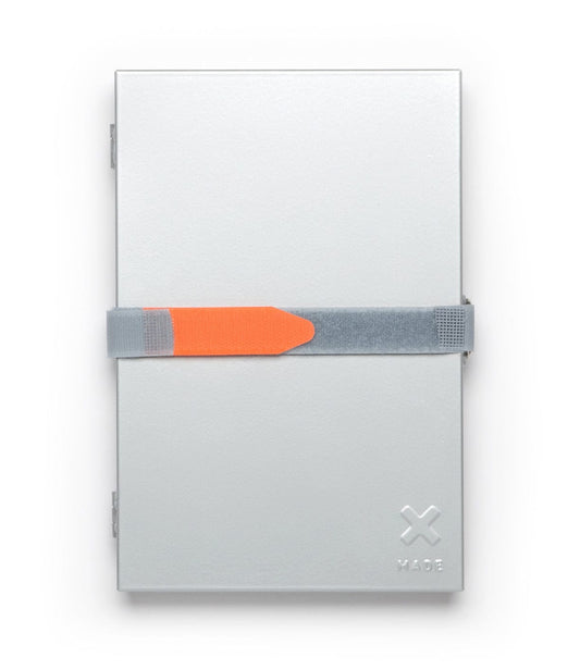 A metallic rectangular box with a gray and orange strap across the front. The box has an embossed X logo and the word MADE in the lower right corner.