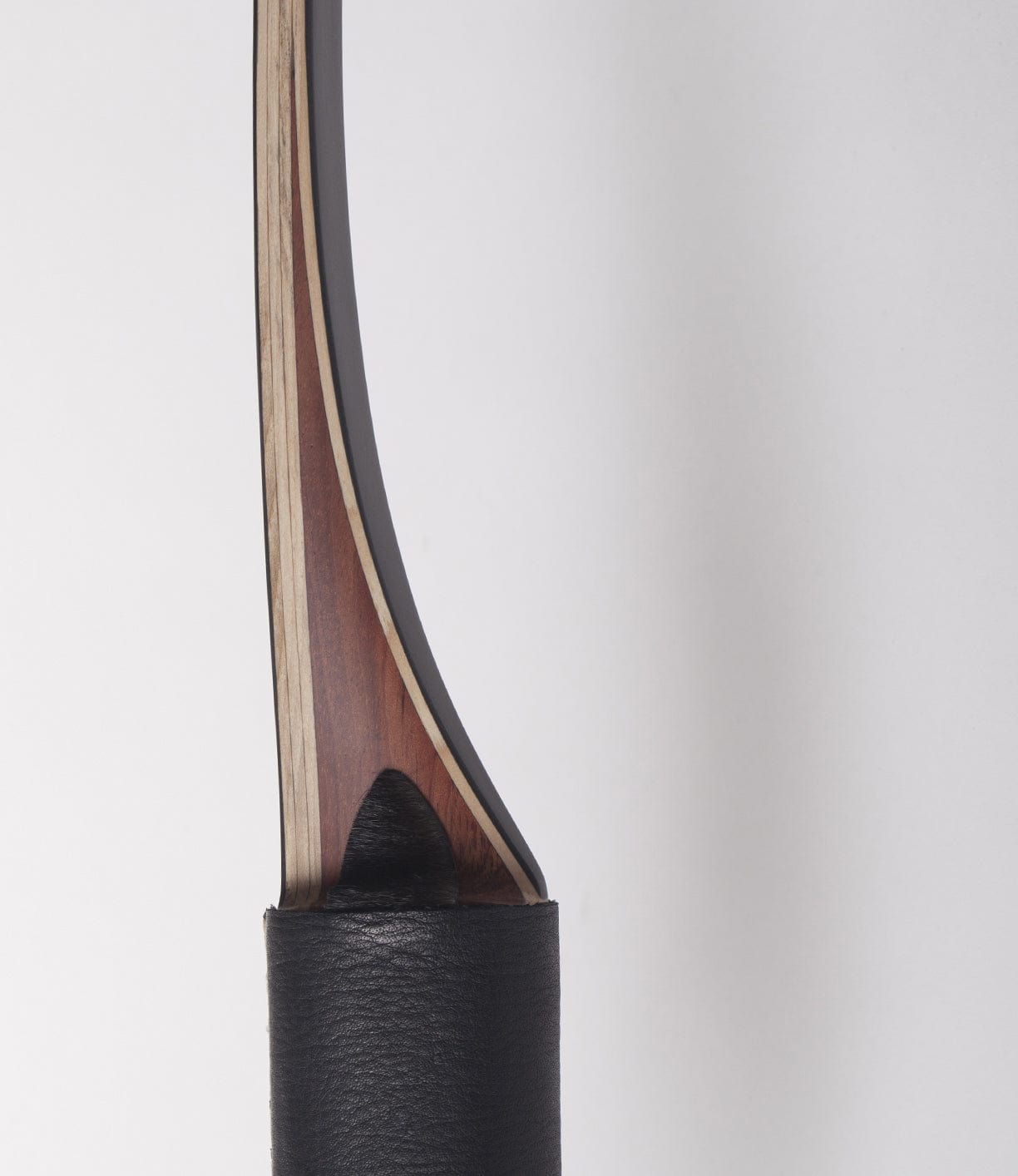 Close-up of the grip and lower limb of a traditional recurve bow, showcasing its wooden core and leather-wrapped handle.