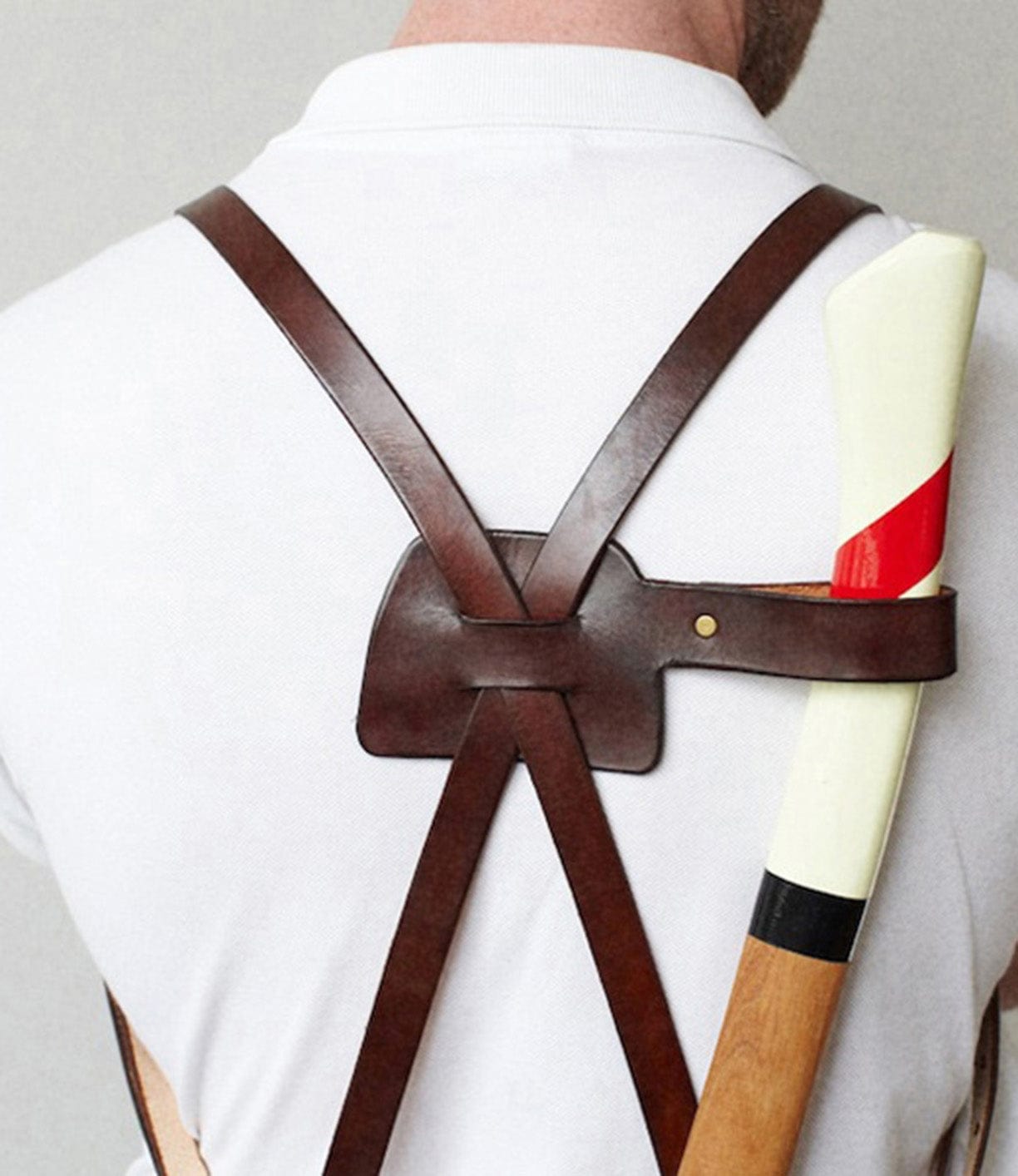 A person wearing a white shirt with brown leather suspenders is shown from the back. The suspenders hold an axe with a white handle, featuring a red stripe and partially visible wooden shaft.