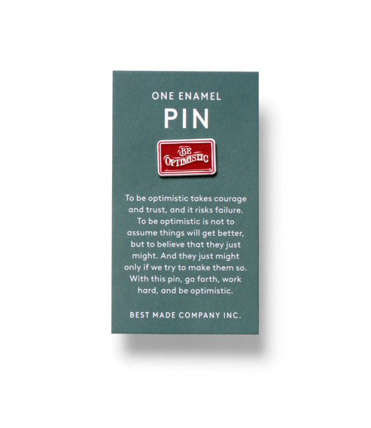 A green card displaying a small red enamel pin with the words Be Optimistic. Text beneath explains the importance of courage and hard work in maintaining optimism. BEST MADE COMPANY INC. is printed below.