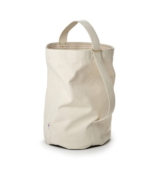 A beige canvas bucket bag with a single handle and a small tag near the base. The bag is standing upright on a white background.