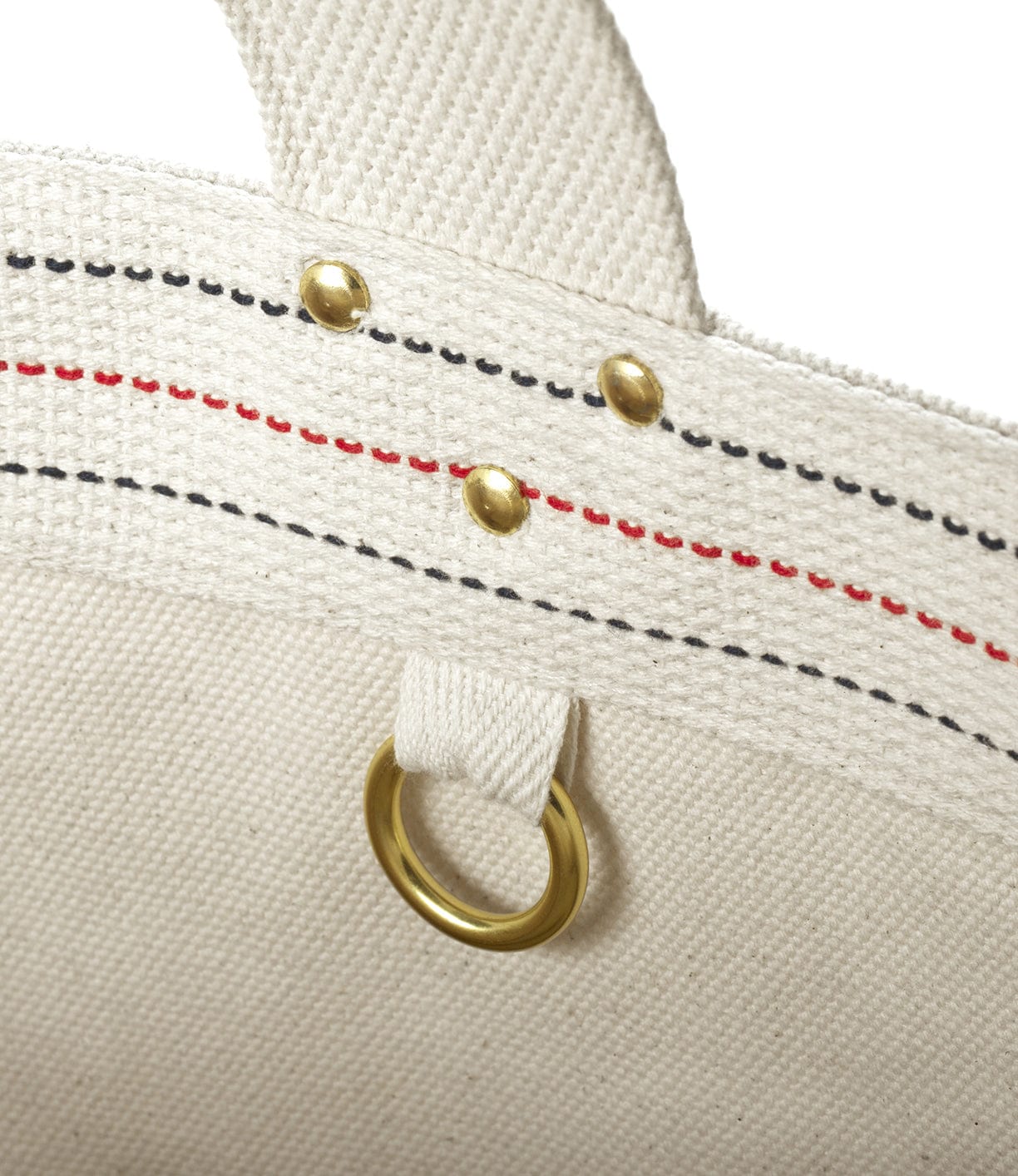 Close-up of a beige fabric bag with brass rivets, a small ring, and red and black stitching details.