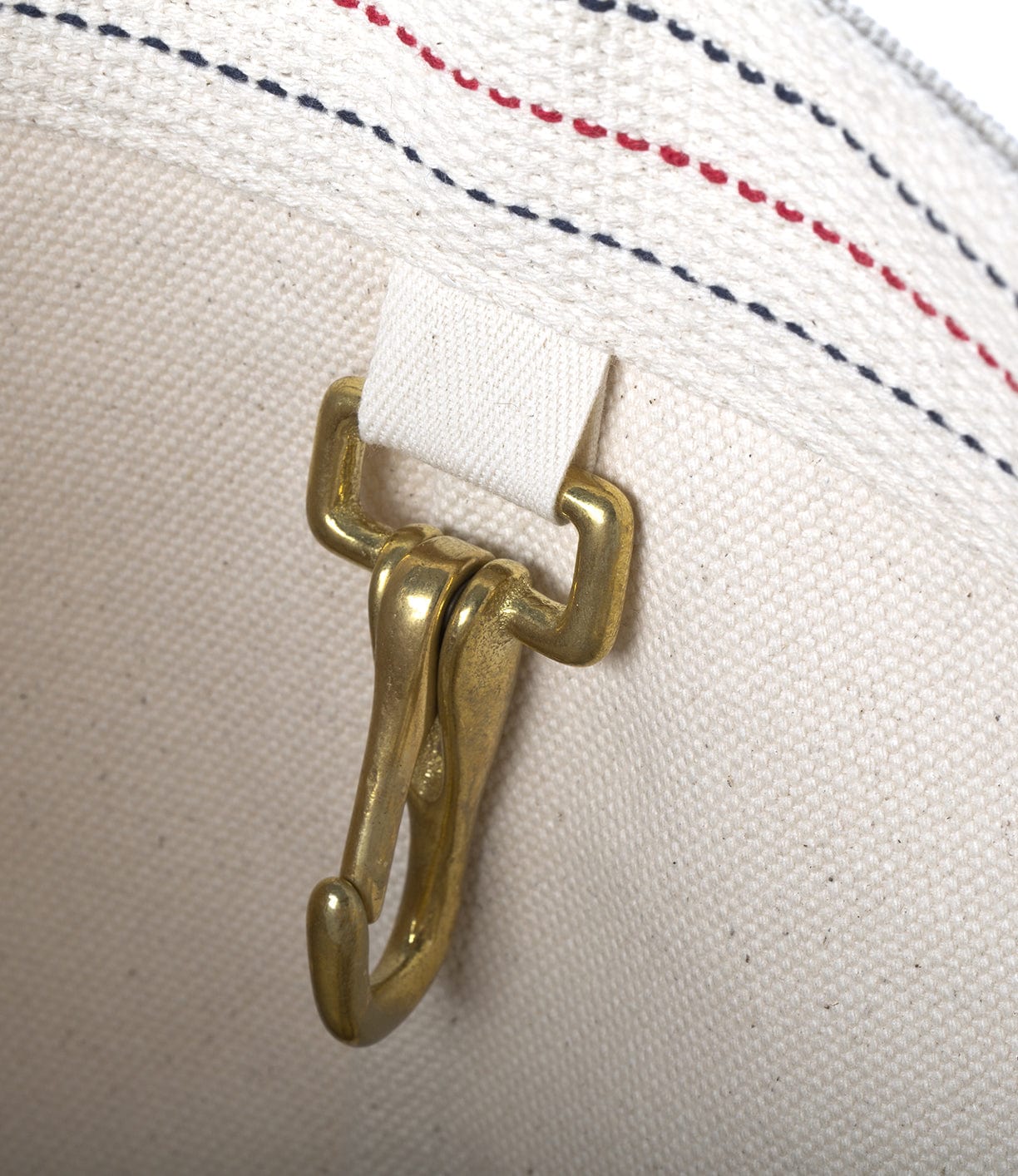 Close-up of a brass hook attachment inside a canvas bag with red and blue stitching.