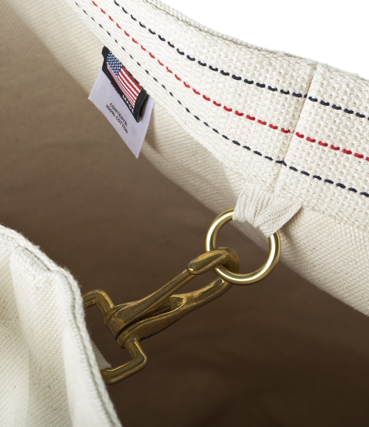 Close-up image of the interior of a canvas bag showing a metal hook clasp attached to a ring and a fabric label with an American flag.