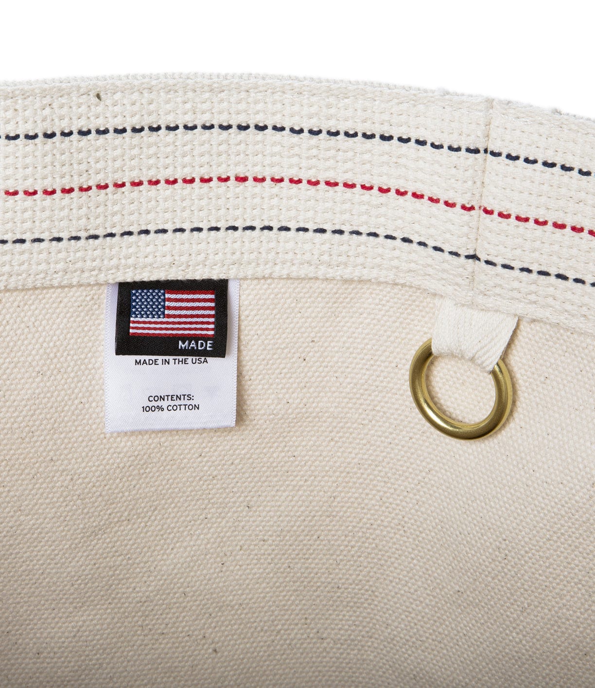 Close-up of a cream-colored cotton item with an American flag tag stating Made in the USA, and indicating Contents: 100% Cotton. A brass grommet and red stitching are also visible.