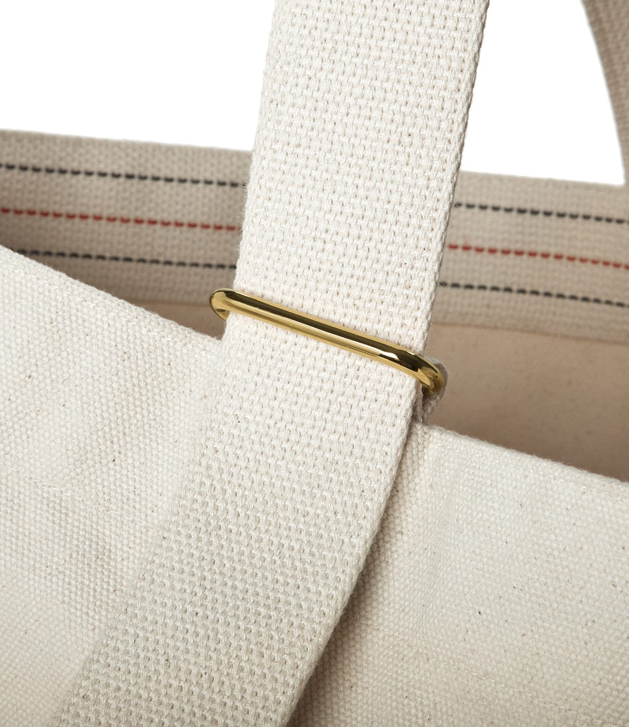 Close-up of a beige canvas bag with a beige strap secured by a gold rectangular ring. Black and red stitching is visible on the strap.