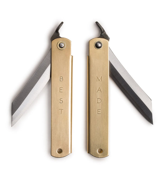 Two brass folding utility knives with blades partially extended. The handles are engraved with the words BEST and MADE respectively.