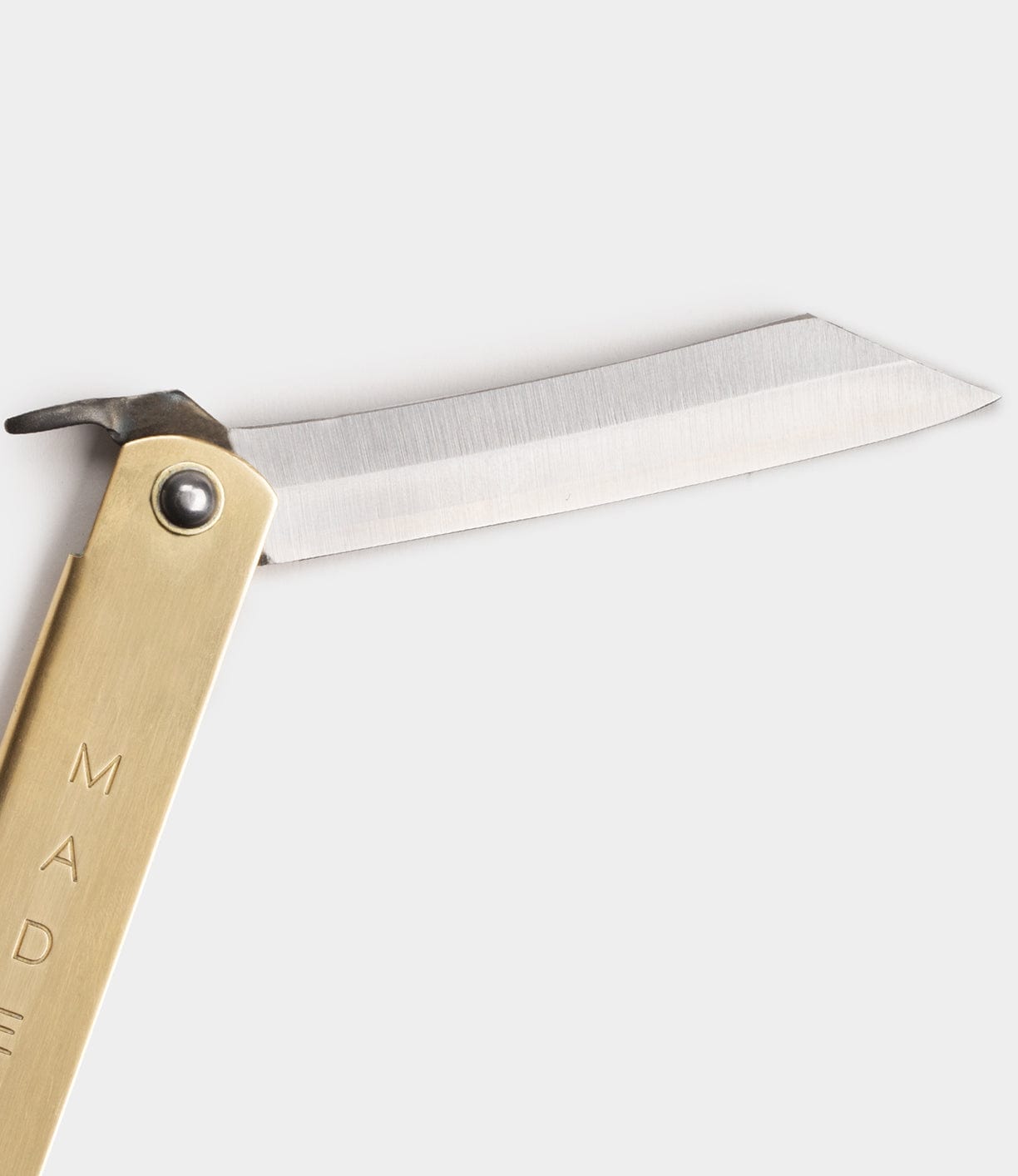 Close-up of an open folding pocket knife with a brass handle and a straight-edged steel blade against a plain background.