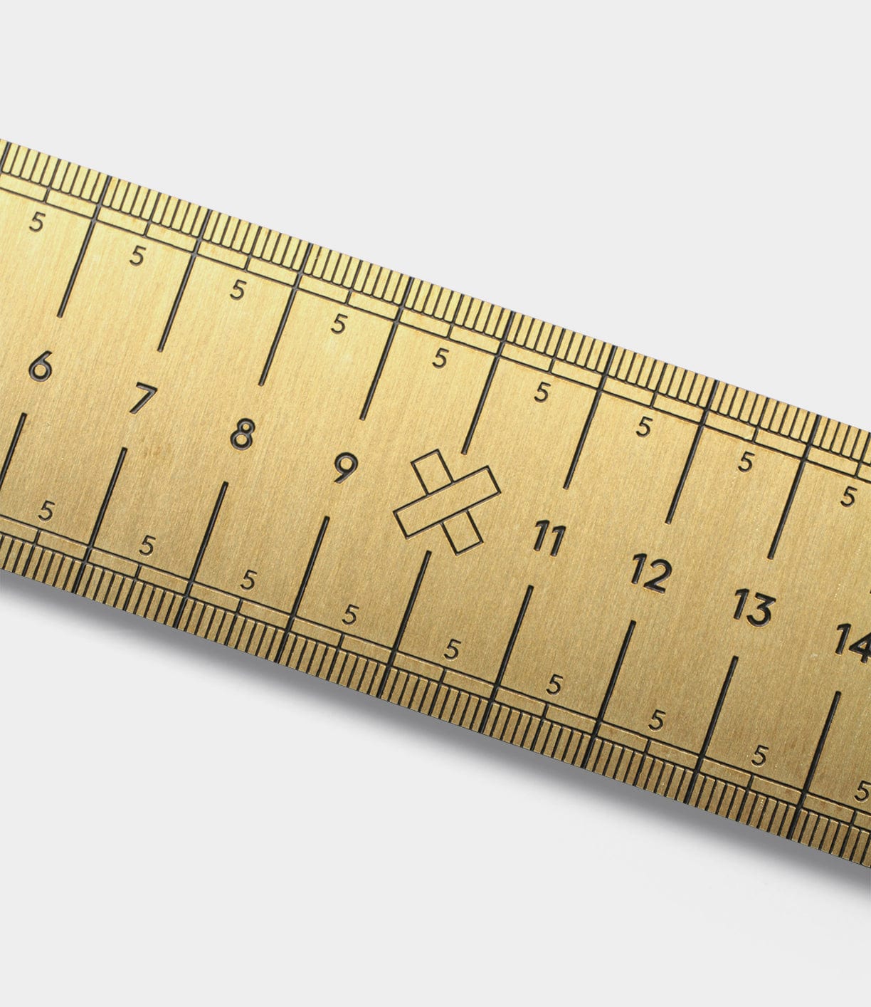 Close-up of a golden metallic ruler with engraved black markings and numbers, showing a small cross symbol near the 9 cm mark.