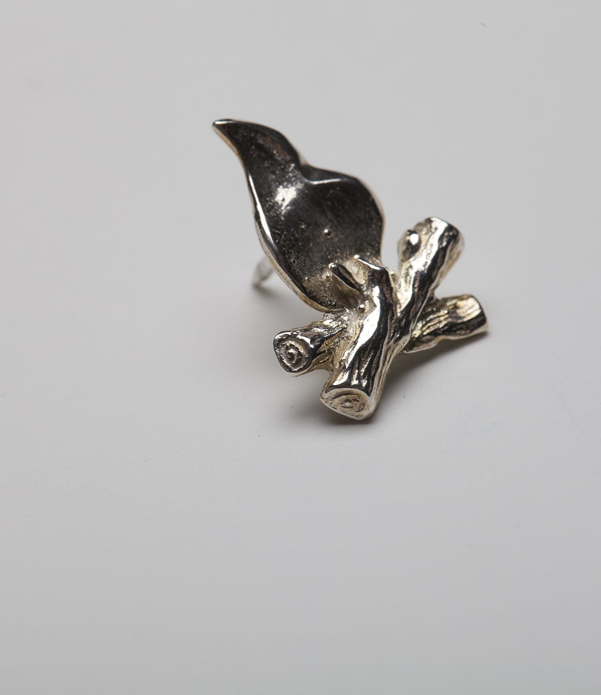 A silver ring featuring a bird perched on a small cluster of branches, set against a plain white background.