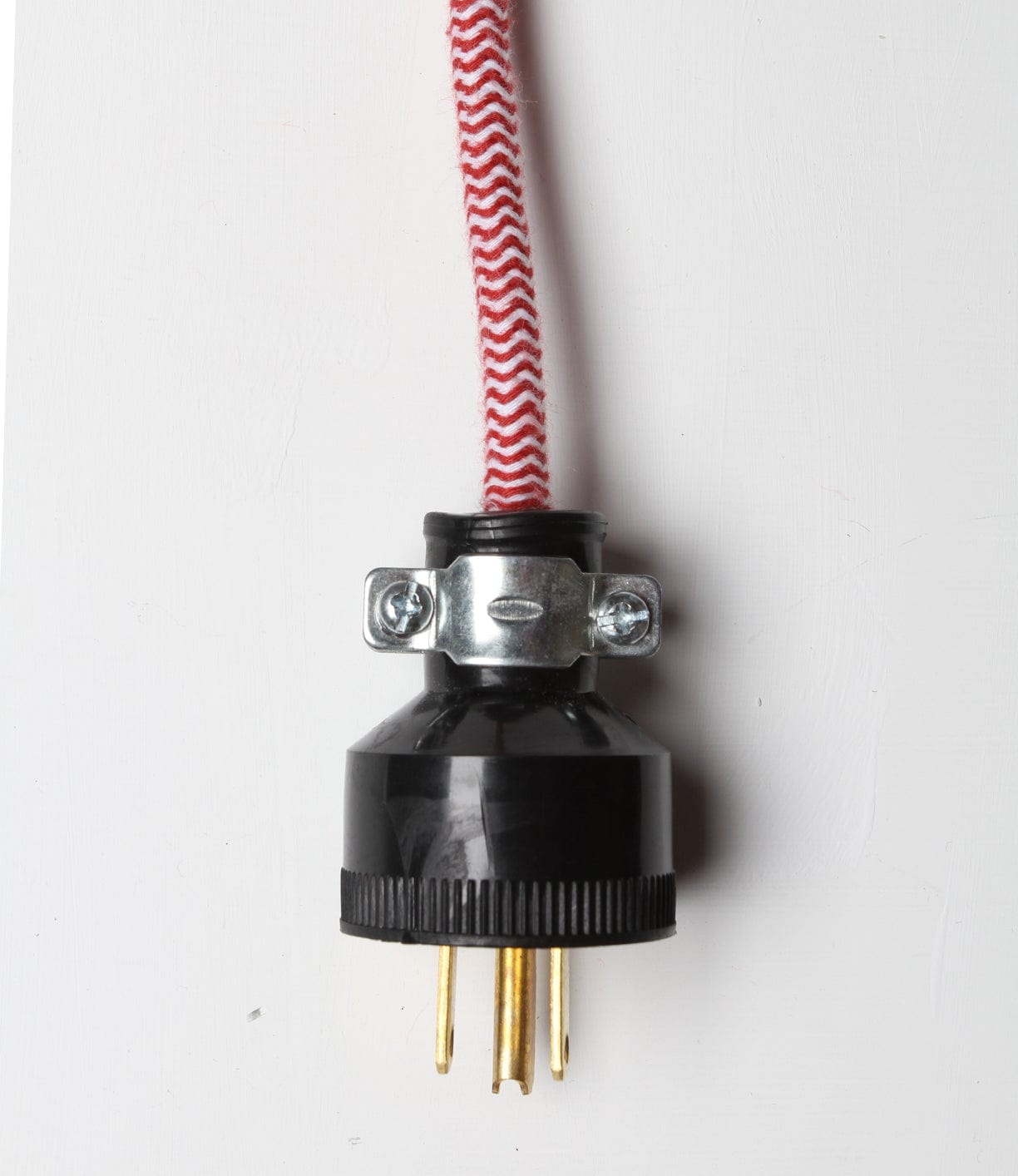 Black electrical plug with three prongs attached to a red and white herringbone-patterned fabric cord.