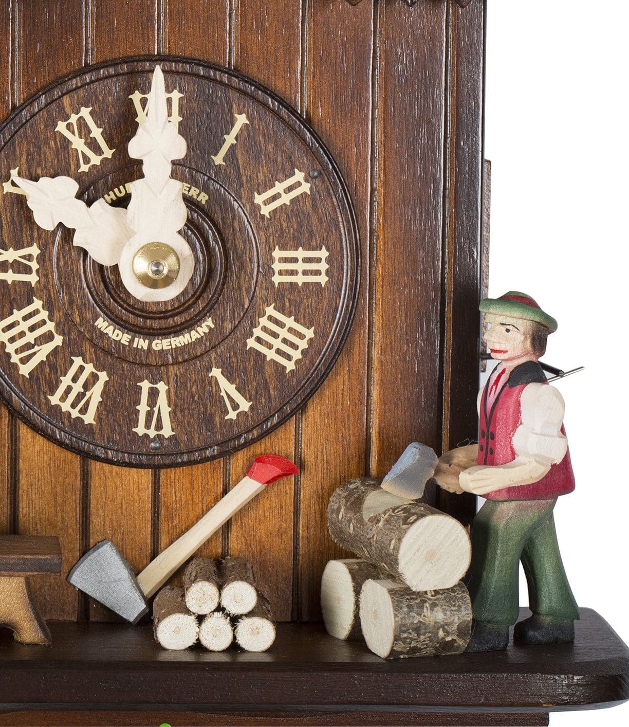 A wooden cuckoo clock featuring an engraved clock face and a small figure of a man chopping logs with an axe. The clock is labeled Made in Germany.