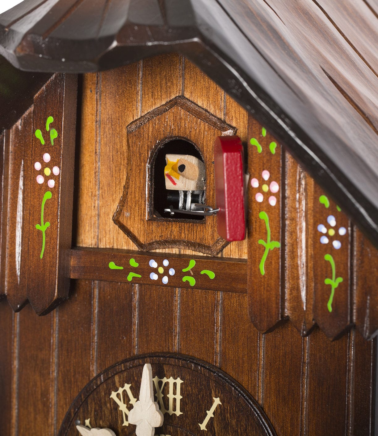 Close-up of a wooden cuckoo clock with decorative floral patterns. A small bird figurine is emerging from the door above the clock face.