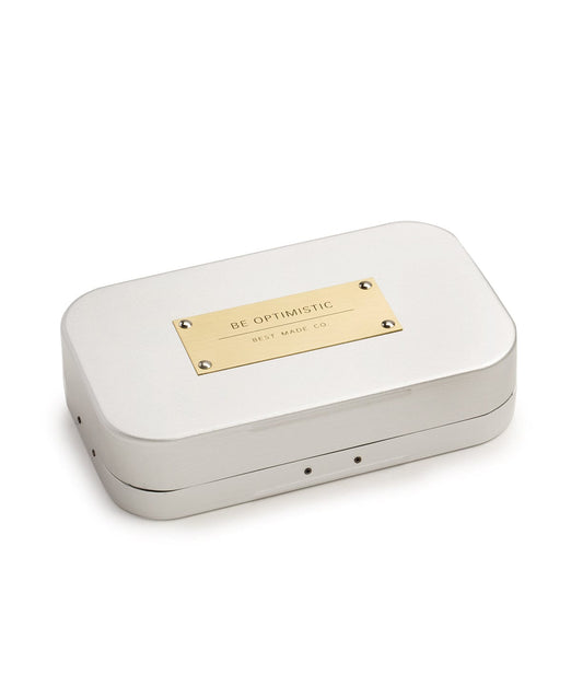 A white rectangular metal tin with a gold plaque reading Be Optimistic and Best Made Co at the center of the lid.