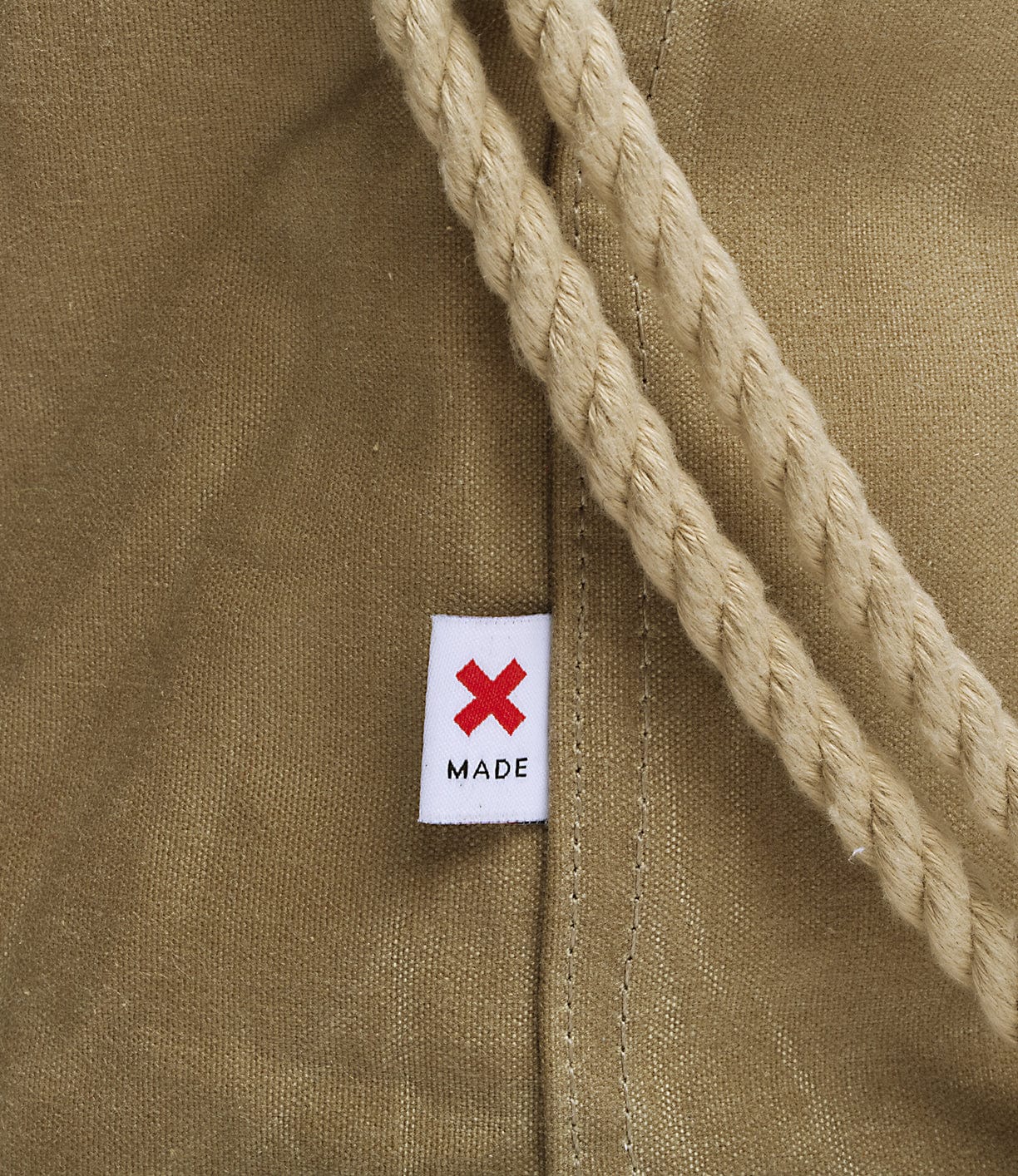 Close-up of a beige fabric with a cream-colored rope and a small white label featuring a red X and the word MADE beneath it.