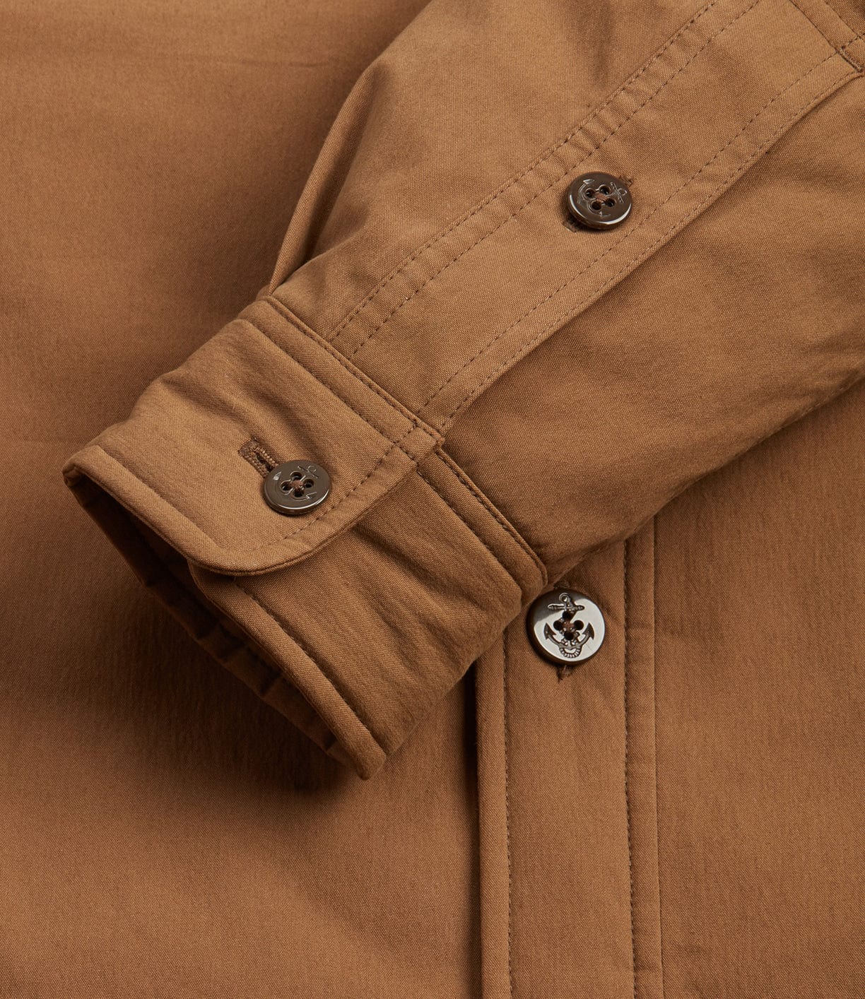 Close-up of a brown long-sleeve shirt cuff with buttoned placket. The fabric appears to be soft with visible stitching details.