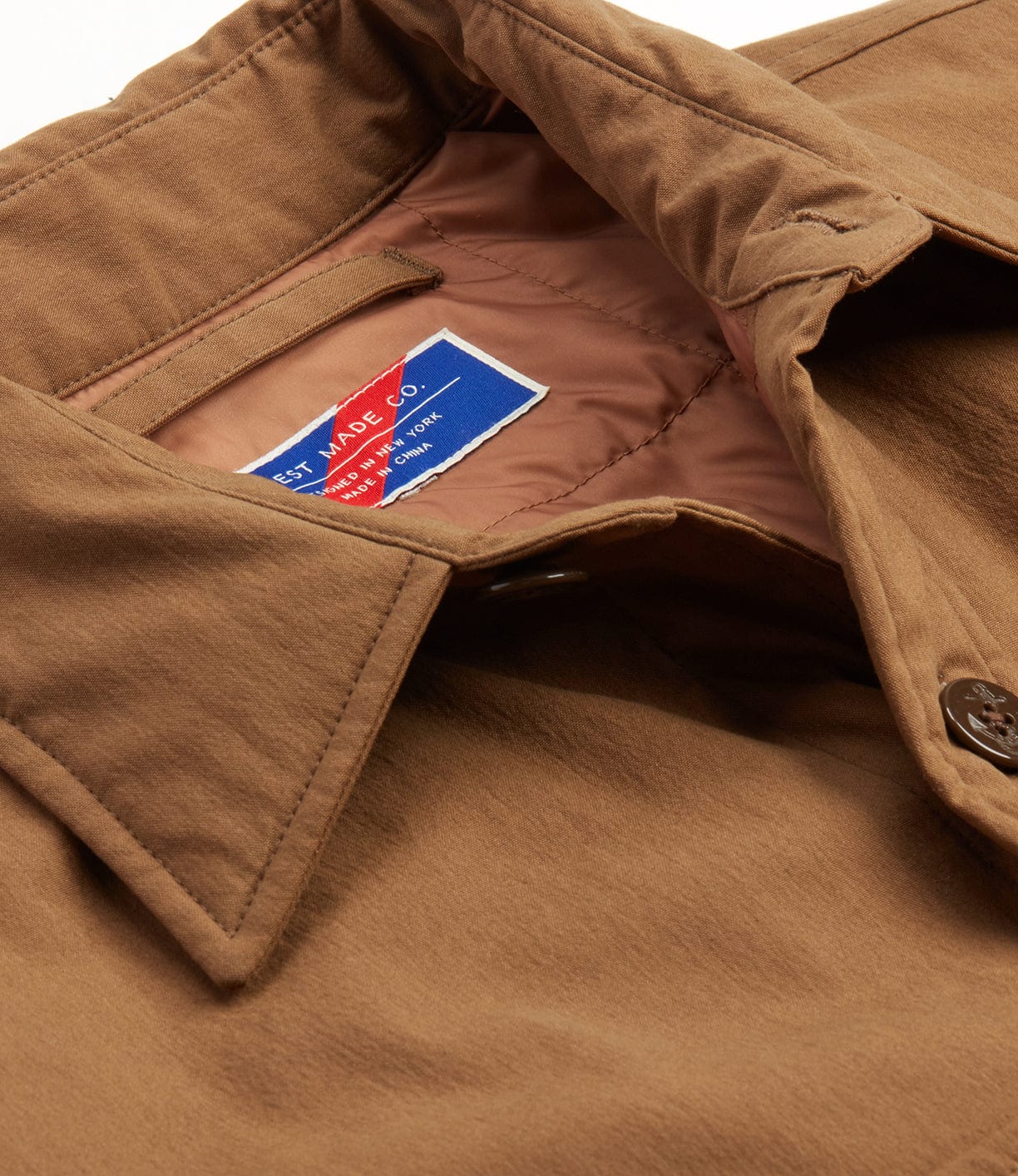 Close-up of a brown jacket with a partially visible blue and red stitched label inside, reading Best Made Co.