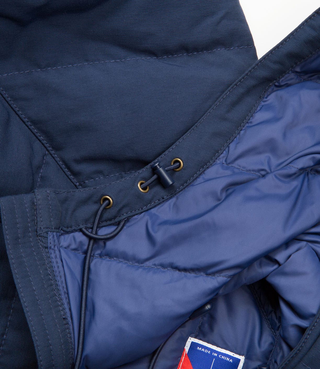 Close-up of a blue quilted jacket showing the interior lining, drawstrings, and a tag indicating it was made in China.