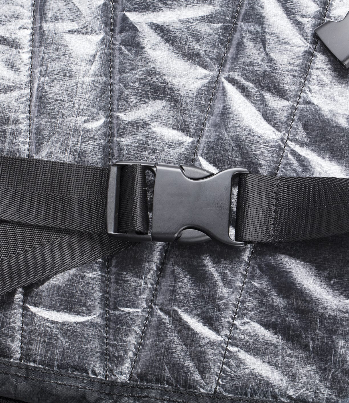 Close-up of a black plastic buckle clasped on a black strap, secured to a silver, textured fabric background.