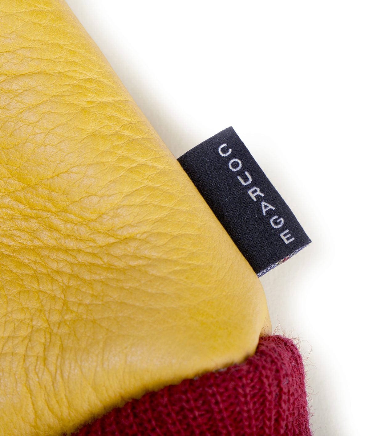 Close-up of a yellow leather item with a black label that has the word COURAGE in white text. The edge of a red knitted fabric is also visible at the bottom.