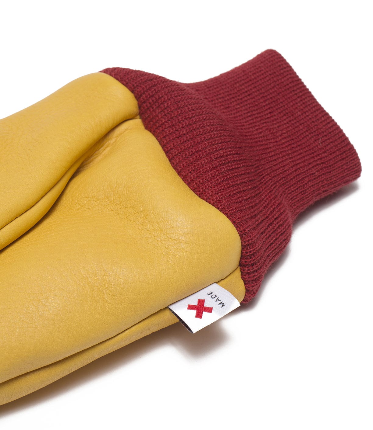 Close-up of a yellow leather glove with a red knit cuff and a white tag featuring a red X symbol.