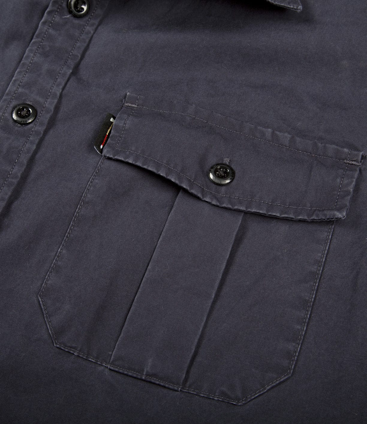 Close-up of a dark-colored shirt with a buttoned flap pocket on the chest. The shirt has visible stitching and black buttons.