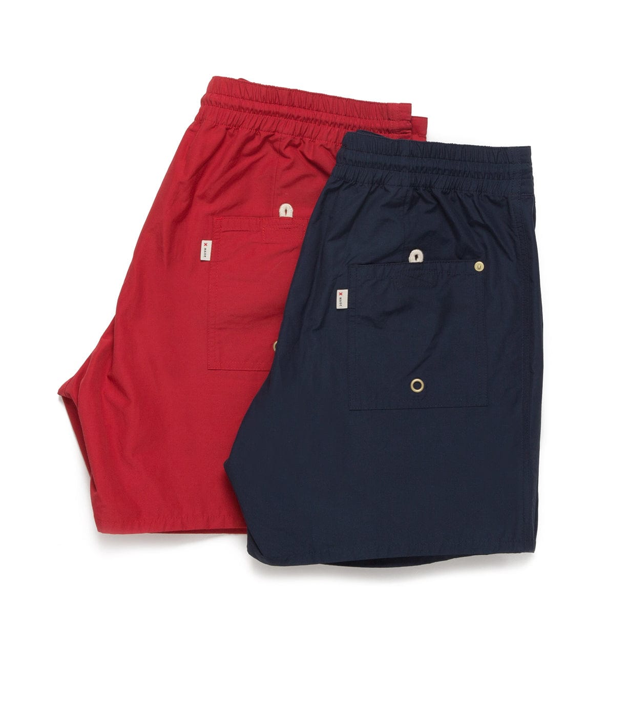 Two pairs of shorts, one red and one navy blue, are laid flat on a white background. Both shorts have elastic waistbands and back pockets with buttons.