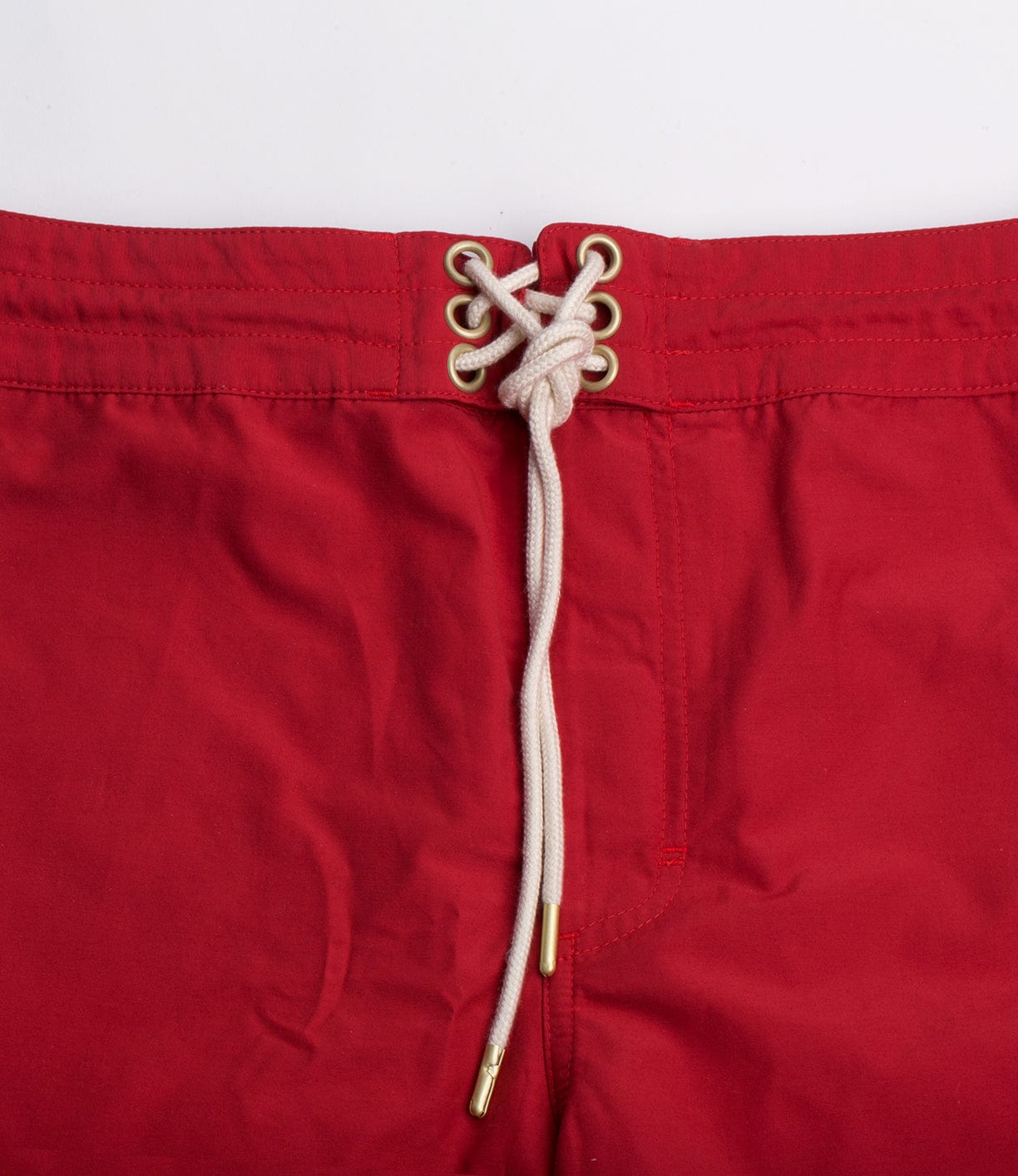 Close-up of a pair of red shorts with a white drawstring threaded through eyelets at the waistband.