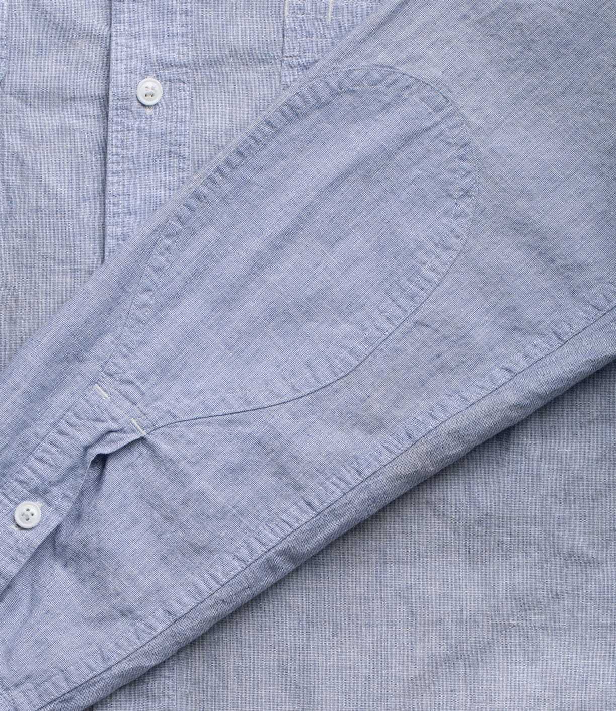 Close-up of a blue long-sleeved shirt sleeve with a buttoned cuff and an oval patch on the elbow area.