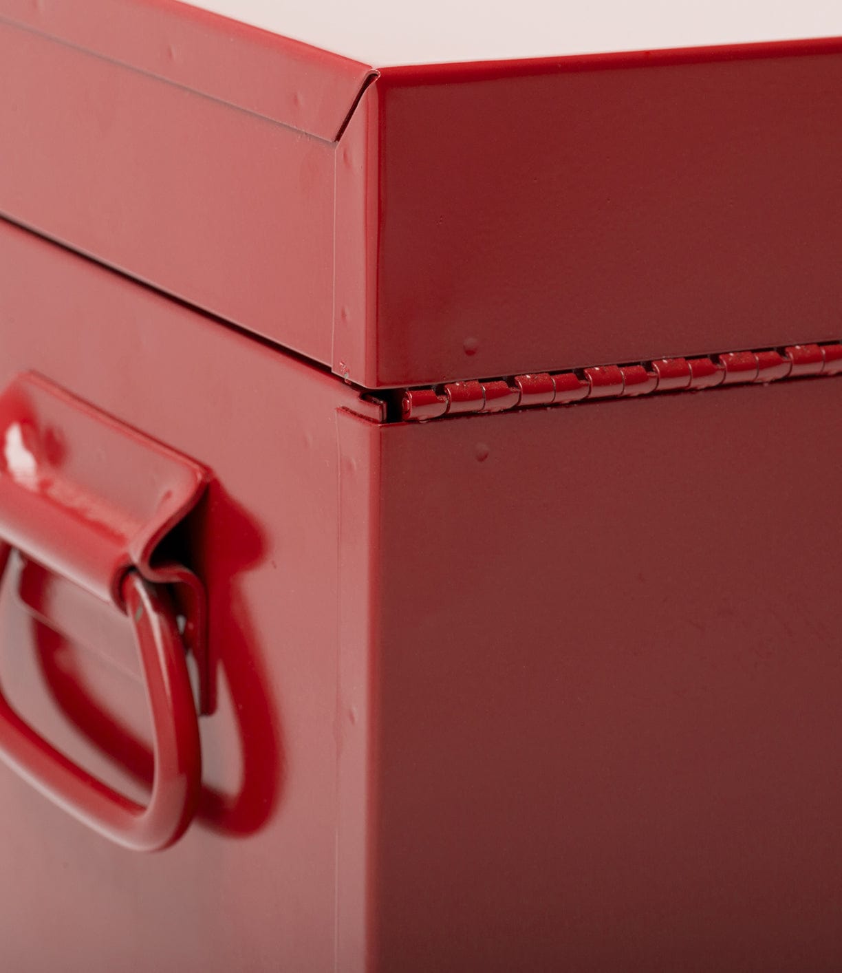 Close-up of a red metal box, showing the corner with a hinge and a handle on one side.