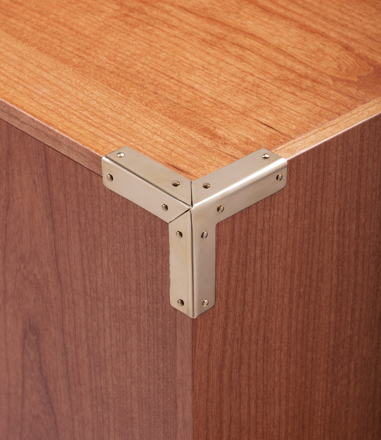 Close-up of a wooden corner with a metallic L-shaped bracket secured by screws, reinforcing the joint of two wooden panels.