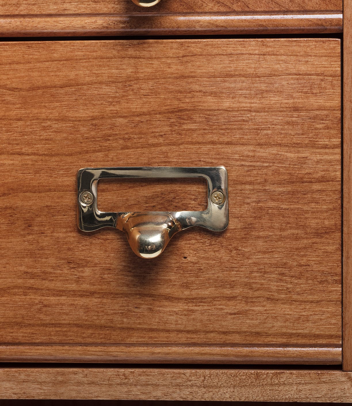 Close-up of a wooden file cabinet with a shiny brass drawer pull and label holder.