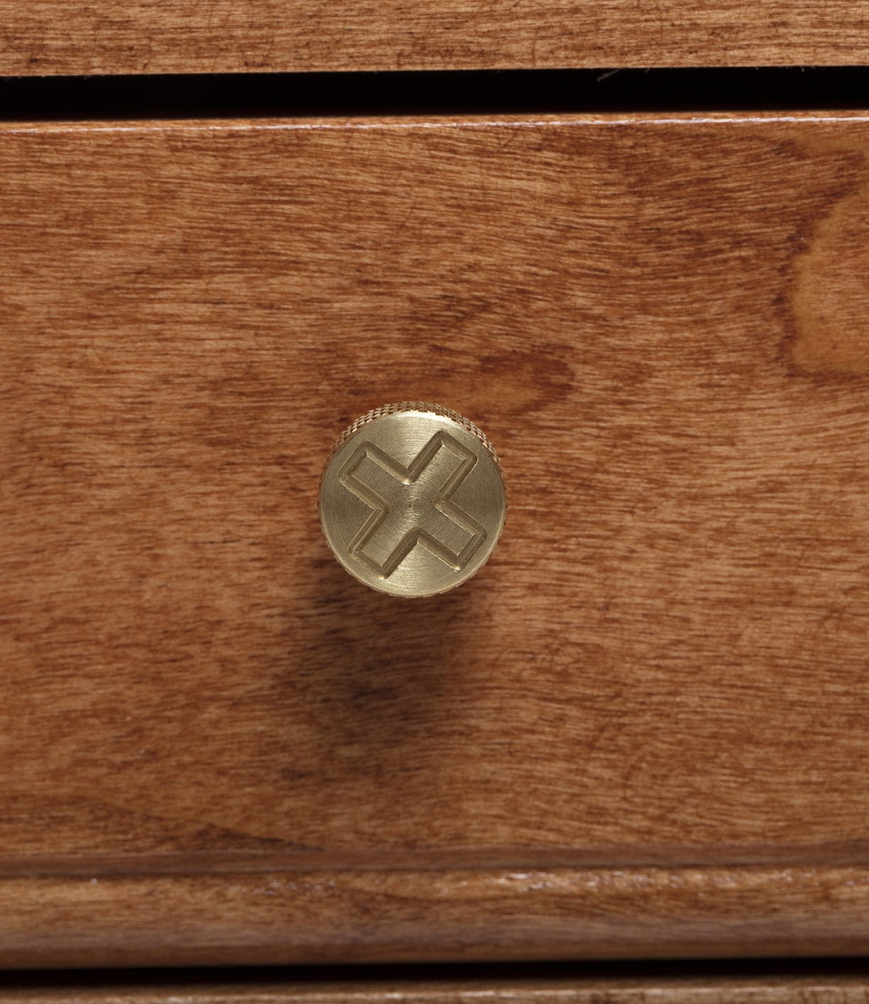 A wooden drawer with a brass knob featuring an engraved cross pattern.