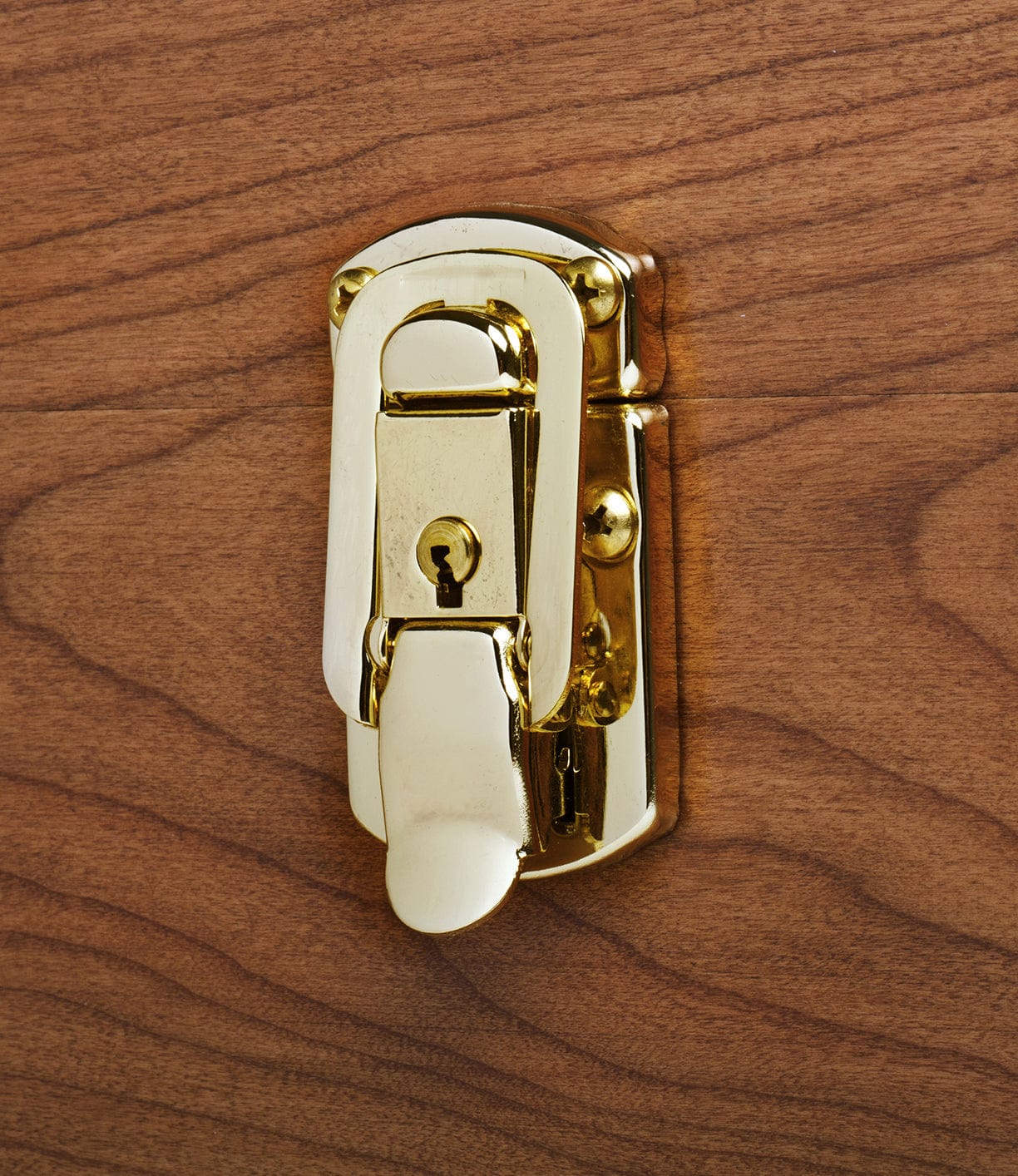 A close-up view of a brass latch with a keyhole mounted on a wooden surface.