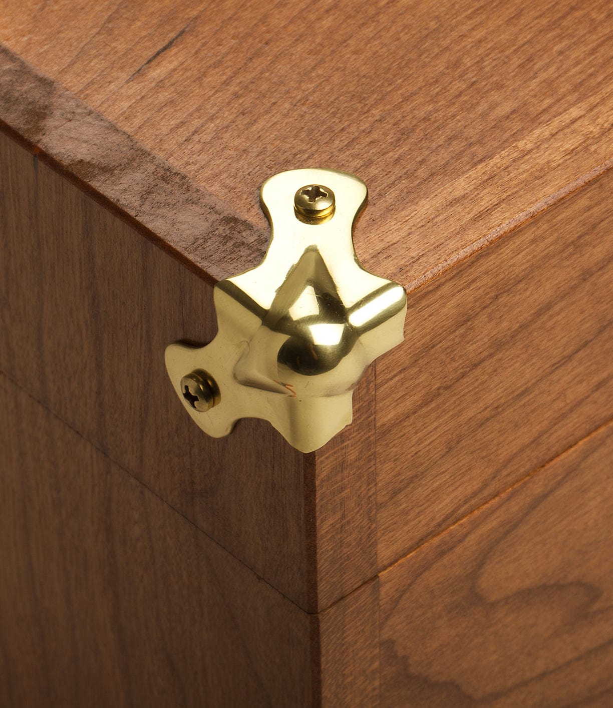 Close-up of a wooden box corner protected by a polished brass corner guard, secured with two screws.