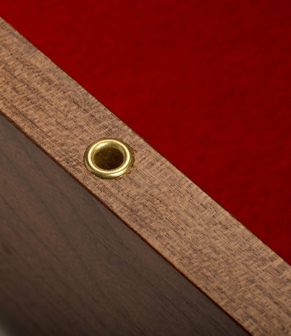 Close-up of a corner of a wooden frame with a brass grommet on a red felt background.