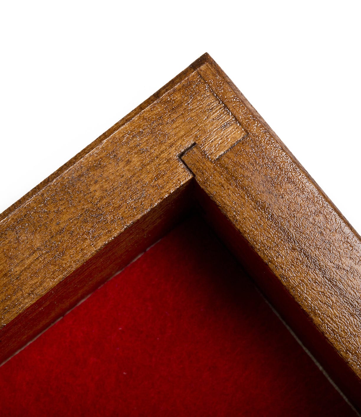 Close-up of the corner of a wooden picture frame with visible joinery, showing the texture of the wood and a red background inside the frame.