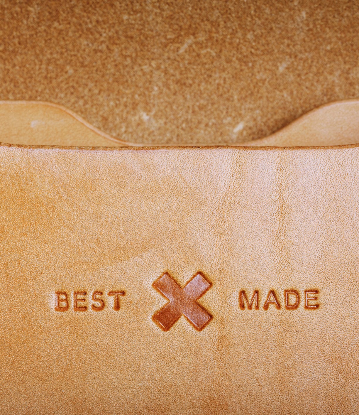 Close-up of tan leather featuring the embossed words BEST MADE with a stylized X in between them. The background appears to be the same leather material.