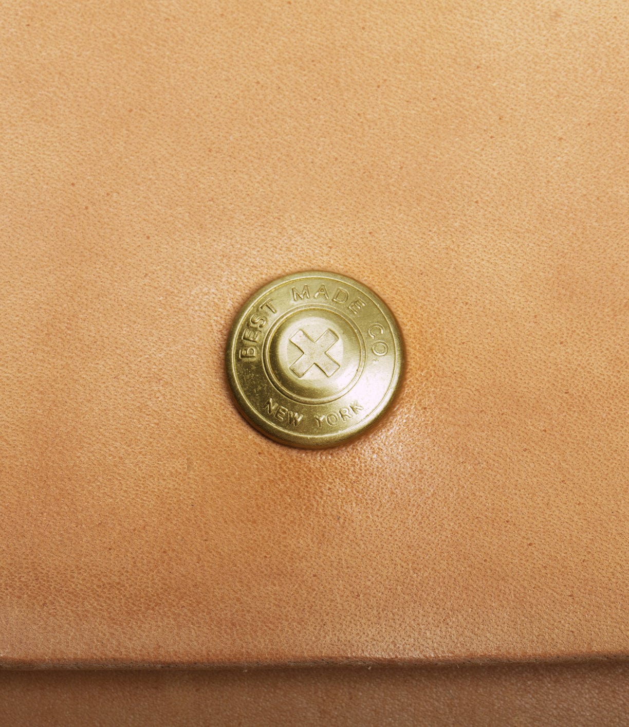 Close-up of a round, brass button on a light brown leather surface, engraved with Best Made Co. New York around the edge.