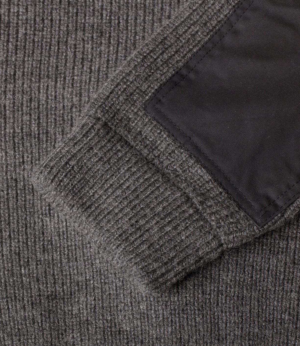 Close-up of a gray, ribbed fabric sleeve with a black rectangular patch sewn onto it.